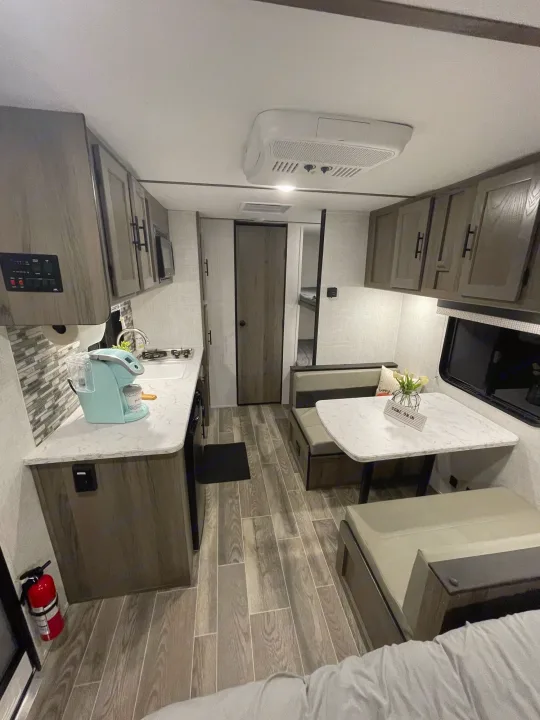 Modern RV rental interior: view of compact kitchen with coffee maker, dinette seating, and wood-look flooring. Functional living space.. Gulf Stream Enlighten 18BH 2022