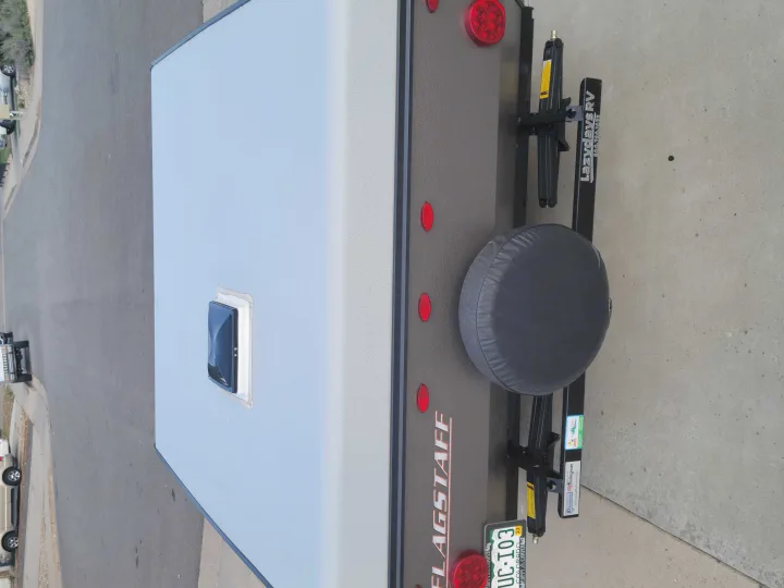 Rear view of an RV rental, a Flagstaff travel trailer with a spare tire and Colorado license plate.. Forest River Flagstaff 2021
