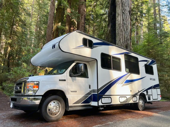 Winnebago Outlook RV rental parked among tall forest trees on a sunny day, ideal for nature travel.. Winnebago Outlook 2019