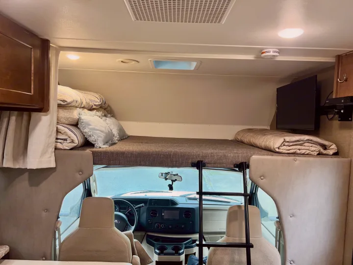 RV rental interior: a comfortable cab-over bunk with bedding, TV, and front cabin. Ready for your next adventure.. Winnebago Outlook 2019