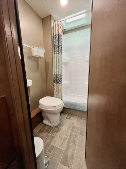 Inside an RV rental: a compact yet functional bathroom with a white toilet, stand-up shower with curtain, and stylish tiled floor.. Winnebago Outlook 2019