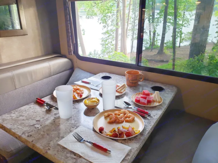 RV rental dinette meal: shrimp, veggies, & watermelon with a serene lake view. Ideal for scenic travel & camping.. Thor Four Winds 2018
