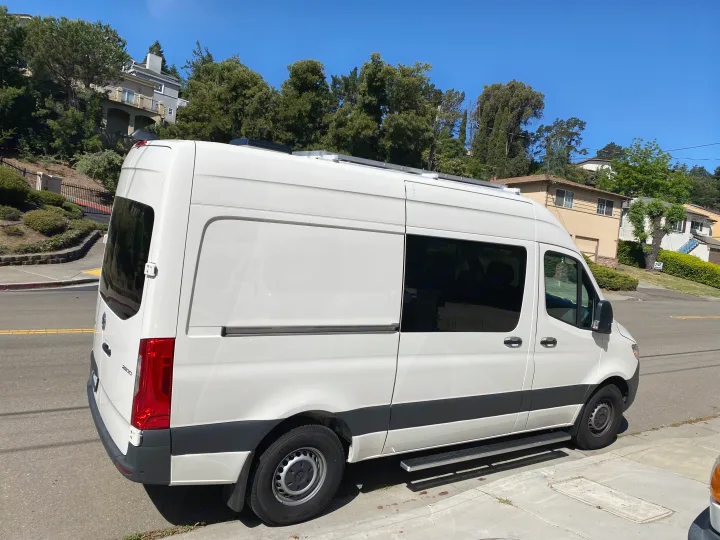 White Sprinter camper van, great for an rv rental, parked on a sunny residential street. Tinted windows & roof features visible.. Vanworks Mercedes Benz Sprinter 2021