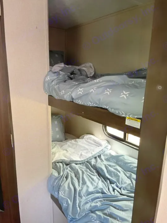RV rental interior: two stacked bunk beds with blue patterned bedding, offering a cozy sleeping area and window.. Keystone RV Springdale 2019