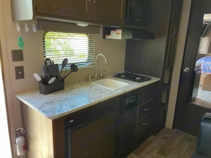 Compact RV rental kitchen, featuring a sink, stove, fridge, and microwave, ready for your next adventure.. Keystone RV Springdale 2019