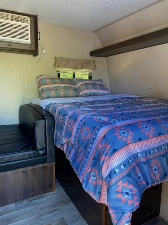 Step into this cozy RV rental bedroom, featuring a vibrant patterned bedspread, window, and air conditioning unit.. Keystone RV Springdale 2019