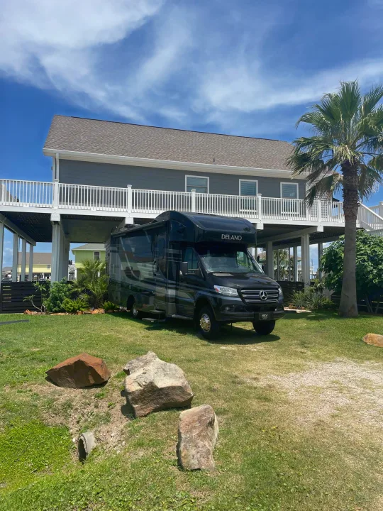 Black Delano motorhome RV rental parked on a green lawn at a modern elevated coastal house under a sunny sky.. Thor Delano Sprinter 2020