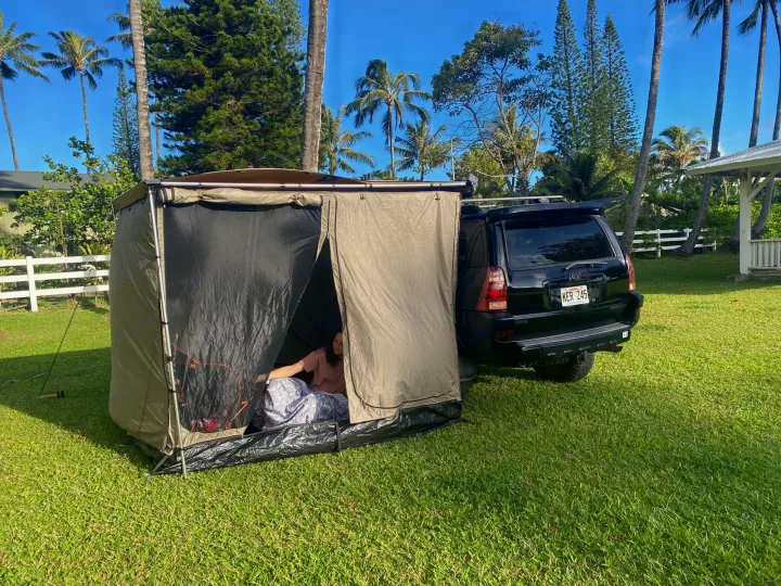 Compact RV rental setup: SUV with attached tent for outdoor camping on a sunny lawn, person inside.. Toyota 4runner 2003