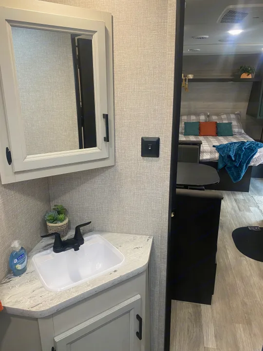 Compact RV rental interior with a functional bathroom vanity, sink, and glimpse into the cozy bedroom area.. Jayco Jay Flight SLX 8 2022
