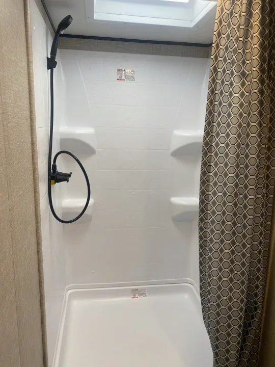 Compact white shower in an RV rental, featuring a handheld showerhead, built-in shelves, and skylight.. Jayco Jay Flight SLX 8 2022