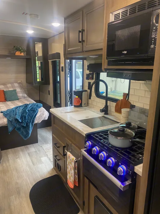 Clean and modern RV rental interior, showing a well-equipped kitchen area with stove & microwave, and a comfortable bed.. Jayco Jay Flight SLX 8 2022