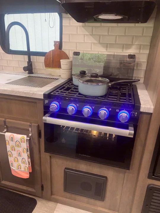 Modern RV rental kitchen featuring a black stove with blue lit knobs, sink, white subway tile, and light blue pots.. Jayco Jay Flight SLX 8 2022