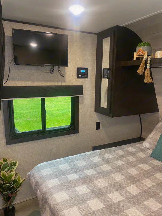 Cozy RV rental interior: bedroom with TV, window to green, solar panel control, and plaid bed. Perfect for trips.. Jayco Jay Flight SLX 8 2022