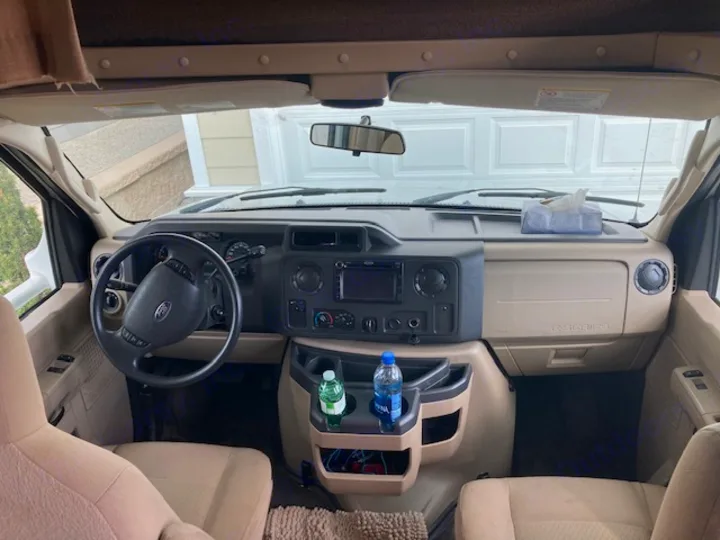 RV rental's clean interior. View of the spacious front cabin with dashboard, steering wheel, and seating.. Coachman Freelander 2013