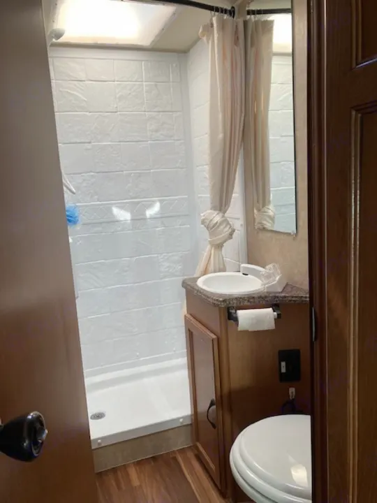 RV rental bathroom featuring a bright shower, sink, toilet, and wood-toned cabinetry. Clean and functional.. Coachman Freelander 2013