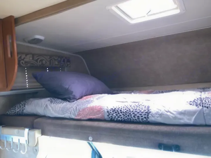 Compact RV rental sleeping area with a bunk bed, patterned comforter, and a purple pillow over a lower bed with a vent.. Coachman Freelander 2013