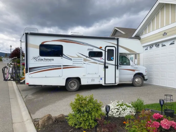 White Coachmen Freelander Class C RV rental with bikes, parked in residential driveway on an overcast day.. Coachman Freelander 2013