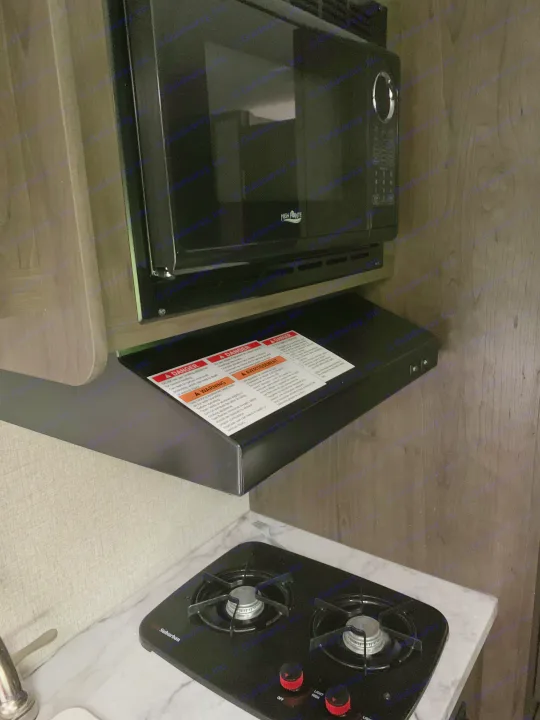 Compact RV rental kitchen features a High Pointe microwave, range hood with warning labels, and a Suburban gas cooktop.. Jayco Jay Flight 2020