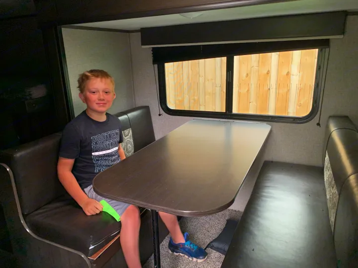 Young boy smiles from the comfy dinette inside this RV rental, showcasing practical, cozy travel space.. Jayco Jay Flight 2020