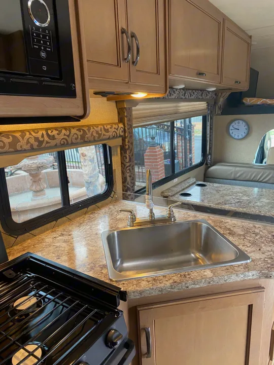 Inside an RV rental: a modern kitchen with a sink, stove, microwave, cabinets, and a cozy dinette by the window.. Thor Four Winds 2019