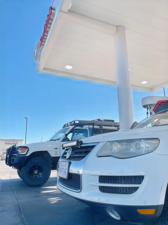 Two white adventure vehicles, an off-road SUV & VW Touareg, refueling at a station, perfect for an RV rental trip.. Custom Camper 1998