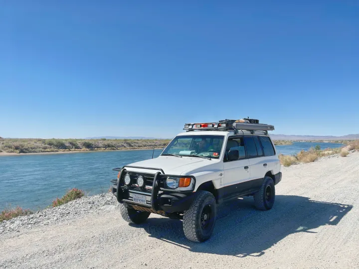 Custom white SUV parked by a river, ready for overlanding. An ideal RV rental for off-road adventure and exploration.. Custom Camper 1998