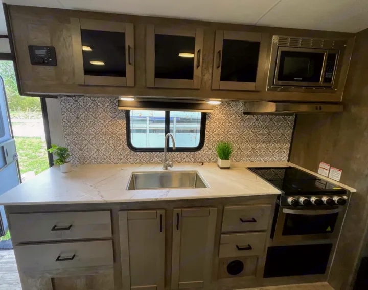Modern rv rental kitchen with sink, stove, microwave, and storage, perfect for your next adventure.. Heartland RVs North Trail 2021
