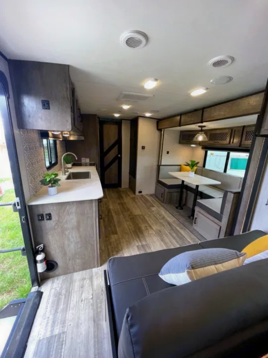 View inside an RV rental, showcasing a full kitchen, dining booth, and living area with a sofa. Modern and functional.. Heartland RVs North Trail 2021