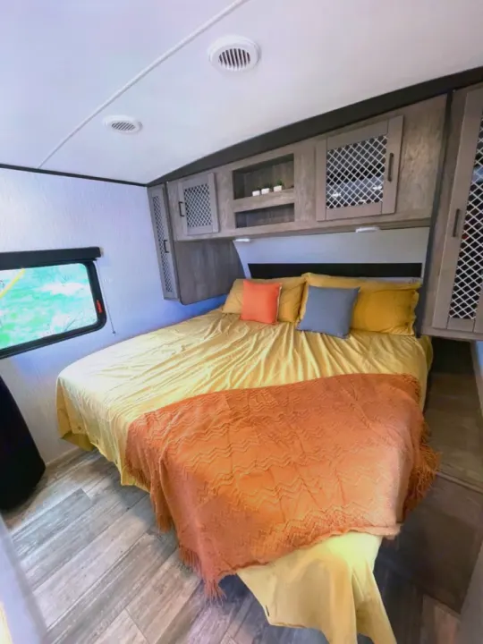 This inviting RV rental bedroom features a comfy bed, overhead storage, and large window. Ideal for your mobile adventures.. Heartland RVs North Trail 2021