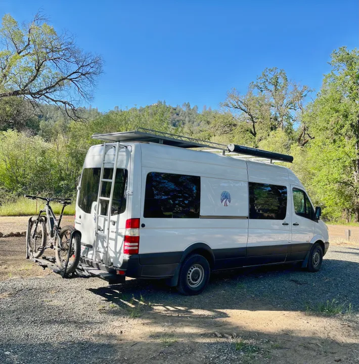 White Sprinter campervan, great for an RV rental, parked on gravel in a lush, treed area with bikes on the rear.. Mercedes-Benz Sprinter 2013