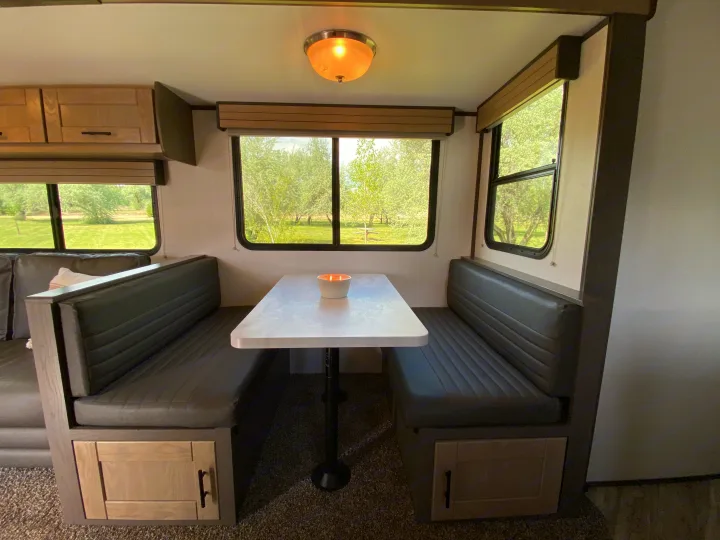 RV rental dinette interior with dark gray booth seating, a white table with a candle, and nature views from large windows.. Cruiser RV M-277BHS 2021