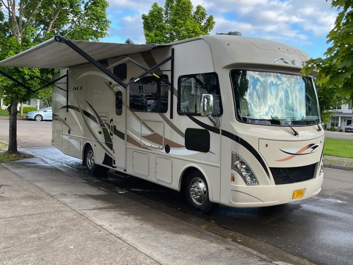 This RV rental, a large motorhome with its awning out, is parked on a wet street. Ideal for your next leisure vehicle trip.. Thor A.C.E. 2017