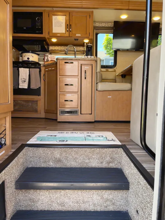 Experience comfort in this RV rental. Full kitchen, dinette, and entertainment area with a 'This Is How We Roll' mat. View from steps.. Thor A.C.E. 2017