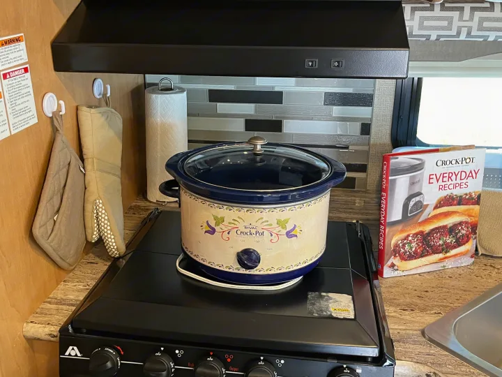 An RV rental kitchen features a Crock-Pot slow cooker on the stove, perfect for easy meals, with a cookbook.. Thor A.C.E. 2017