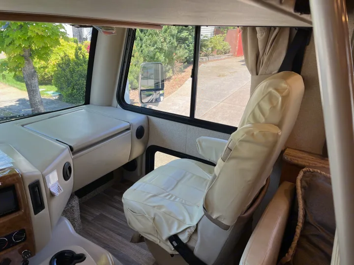 RV rental interior: The driver's seat & cockpit, with a treelined street visible through the front window.. Thor A.C.E. 2017