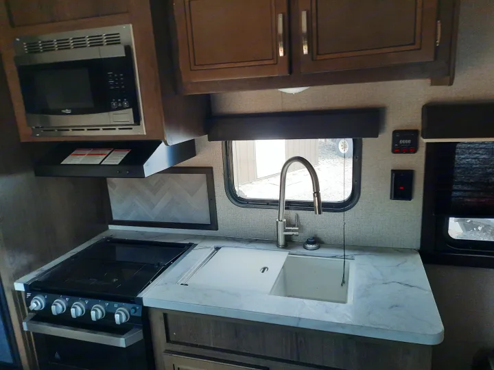 Inside this RV rental, a well-equipped kitchen with a microwave, gas cooktop, sink, and overhead cabinetry.. Jayco Jay Flight SLX 2019