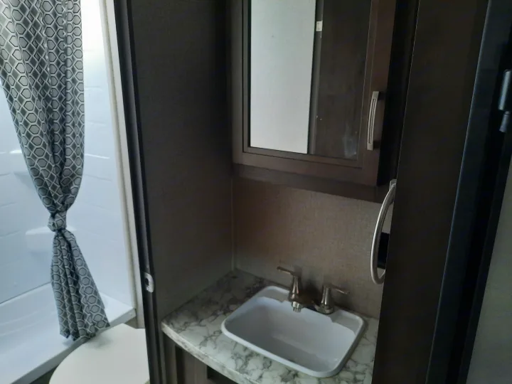 Compact RV rental bathroom with a patterned shower curtain, sink, and mirror, designed for travel comfort.. Jayco Jay Flight SLX 2019
