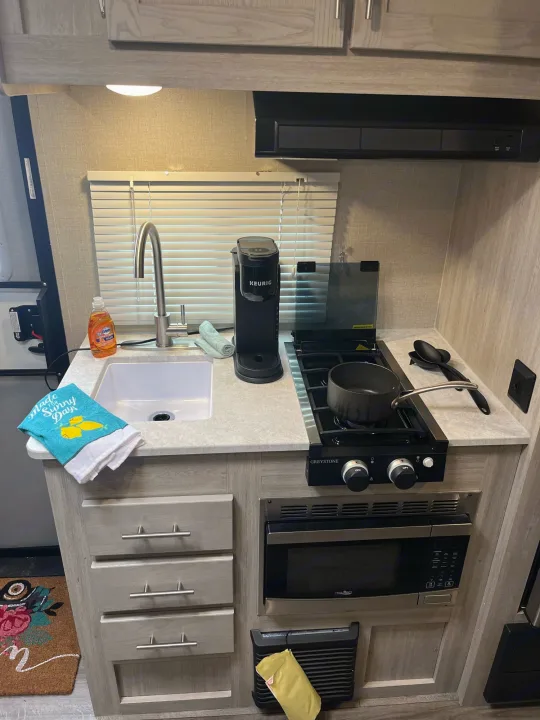 Compact RV rental kitchen features a sink, Keurig, two-burner stove with pot, microwave, and storage drawers.. Coachmen Catalina Summit Series 7 2022
