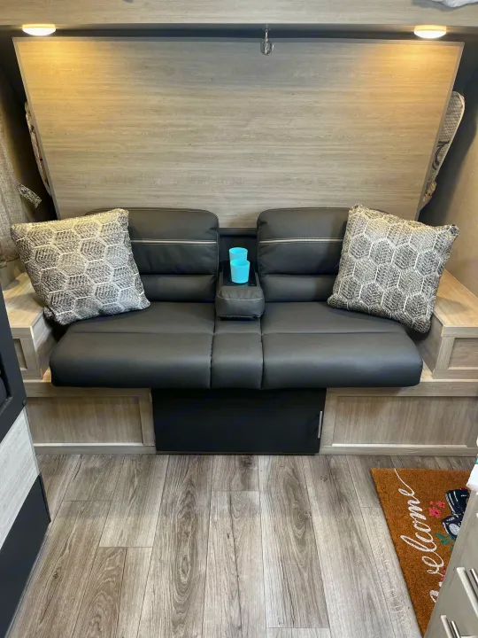 Comfortable RV rental seating area with black sofa, patterned pillows, console, and wood-look floor.. Coachmen Catalina Summit Series 7 2022