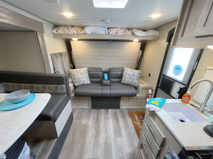 RV rental interior showcasing a light wood and grey color scheme. Features a convertible sofa/bunk, dinette, and kitchen.. Coachmen Catalina Summit Series 7 2022