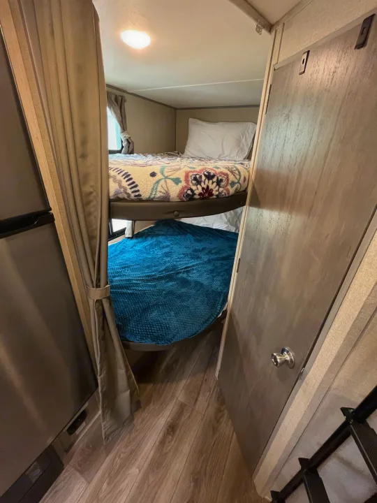 Explore this comfy RV rental interior with practical bunk beds, a fridge, and a door for compact living.. Coachmen Catalina Summit Series 7 2022