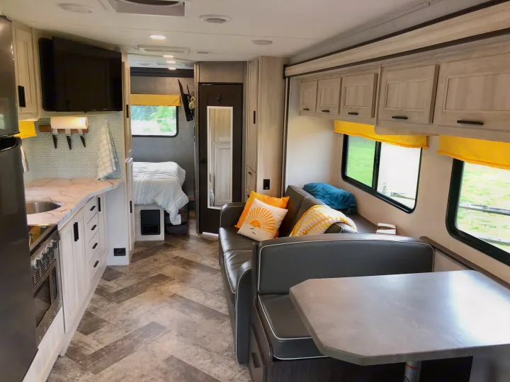 Explore this modern rv rental interior with a bright kitchen, dining booth, and bed area, perfect for travel.. Forester LE 2020