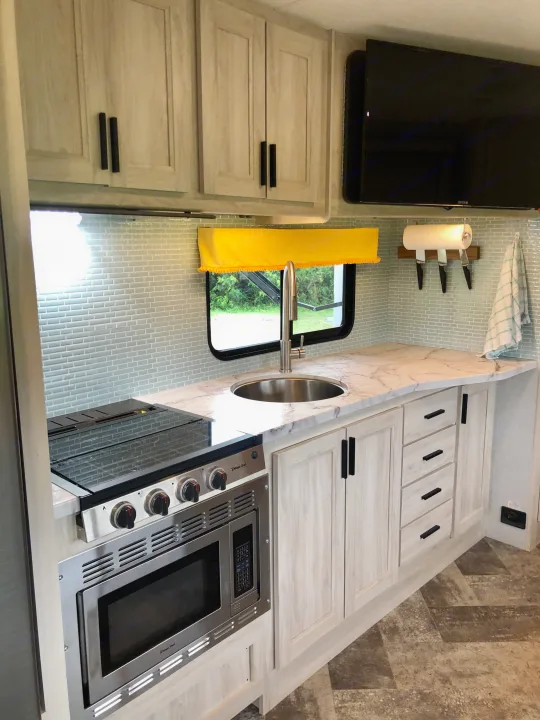 Bright RV rental kitchen with modern light wood cabinets, blue subway tile, stainless appliances, and marble-look counters.. Forester LE 2020