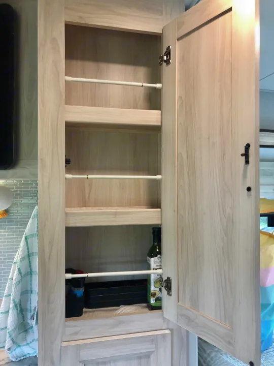 Organized RV rental pantry with light wood shelves and tension rods securely holding items like avocado oil, perfect for travel.. Forester LE 2020