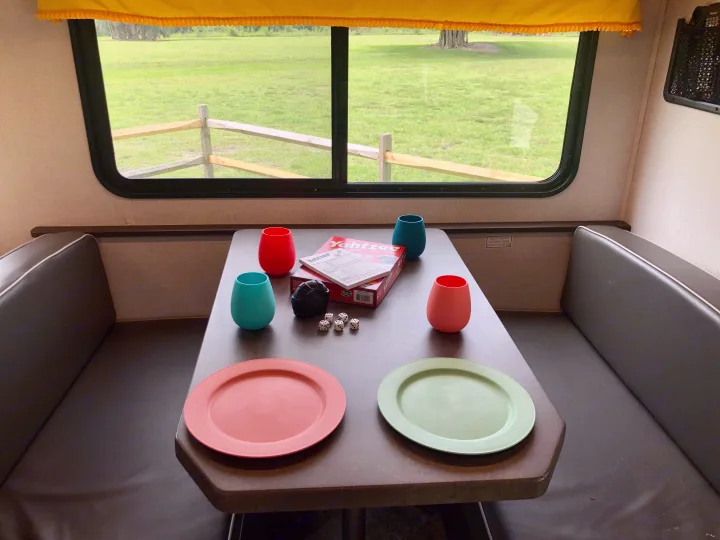 An rv rental dinette with a Yahtzee game ready for play, colorful cups & plates, and a scenic view of a field.. Forester LE 2020