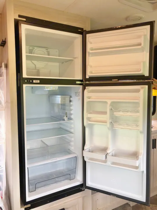 This empty, clean refrigerator in an RV rental is ready for your adventure's food supplies, offering ample storage space.. Forester LE 2020