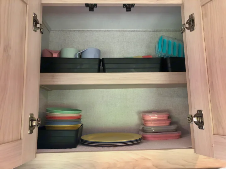 Organized RV rental kitchen cabinet with colorful cups, plates, and stackable containers for efficient use of space.. Forester LE 2020