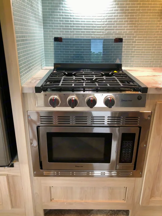 RV rental kitchen: stainless Magic Chef gas cooktop, microwave, and light blue subway tile backsplash.. Forester LE 2020