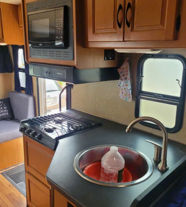 RV rental interior: a compact kitchenette with microwave, stove, sink, and adjacent dinette seating. Ideal for travel cooking.. Thor Majestic 2017