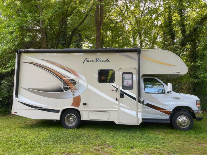 A beige Four Winds Class C RV is parked on green grass. This motorhome is perfect for your next rv rental adventure.. Thor Four Winds 2018